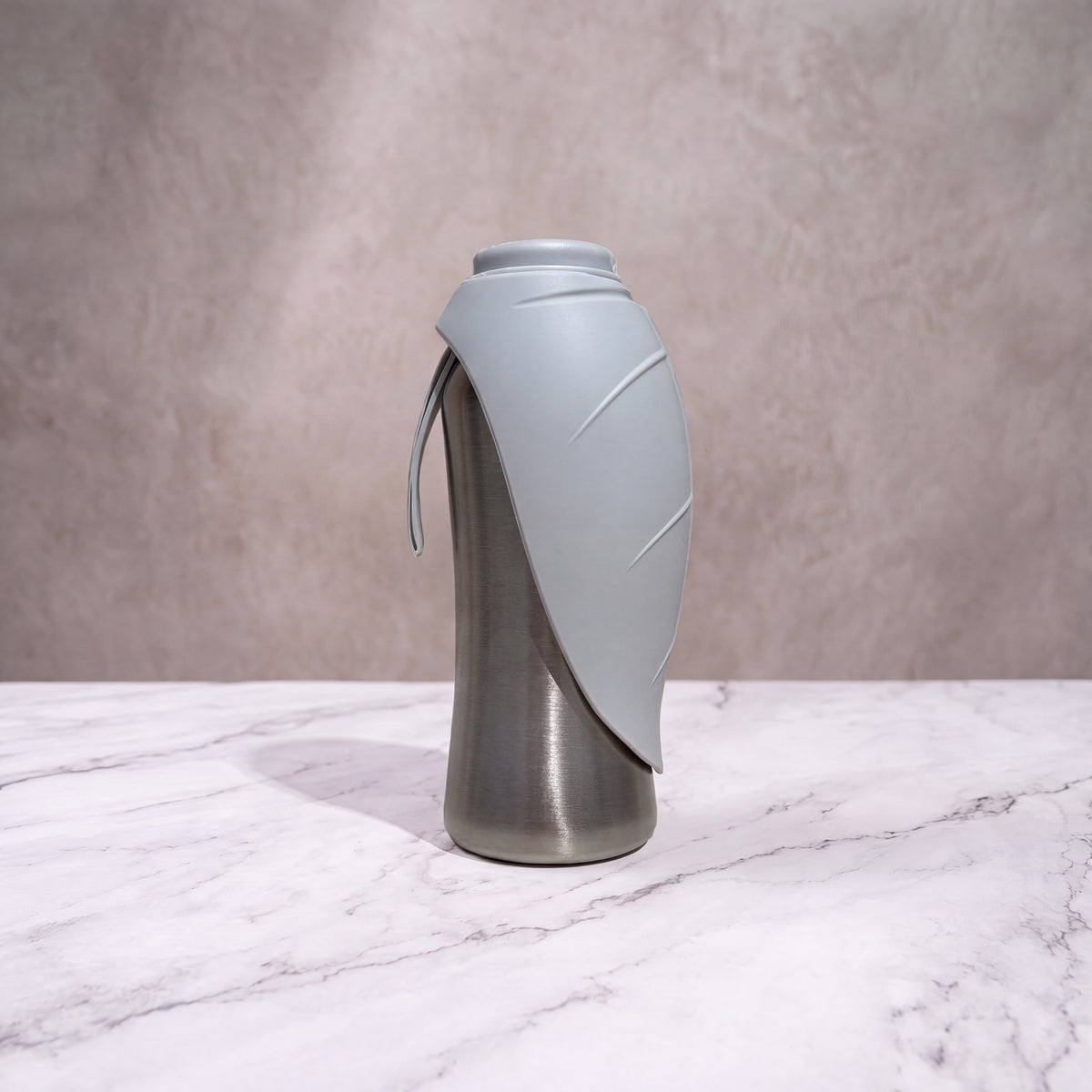 Gourde isotherme pour chien grise et inox de 750ml debout avec son écuelle feuille repliée sur fond marbré.