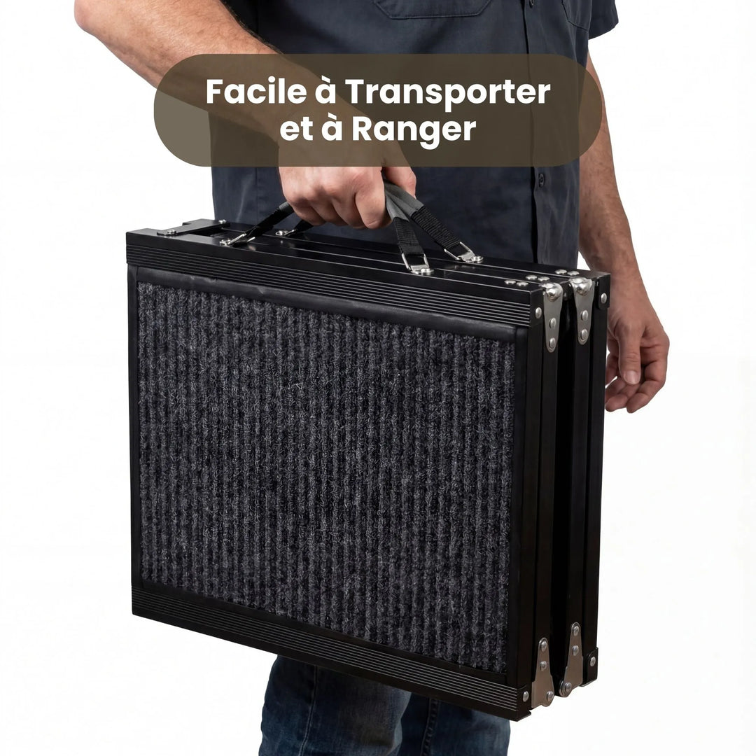 Une personne transporte facilement une rampe pour chien pliée à l'aide de sa poignée renforcée à côté du coffre d'une voiture, illustrant la portabilité et le confort de transport.